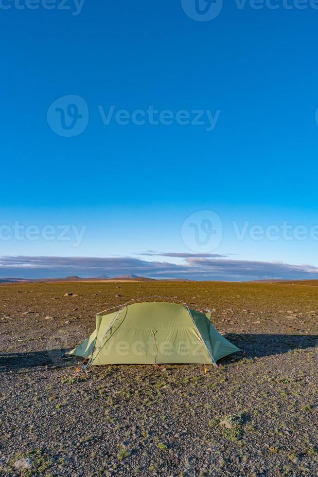 Icelandic landscape of the deadliest volcanic desert in Highlands, with stones and rocks thrown by volcanic eruptions and lonely green hiking tent of a hiker, Iceland, summer, blue sky. photo