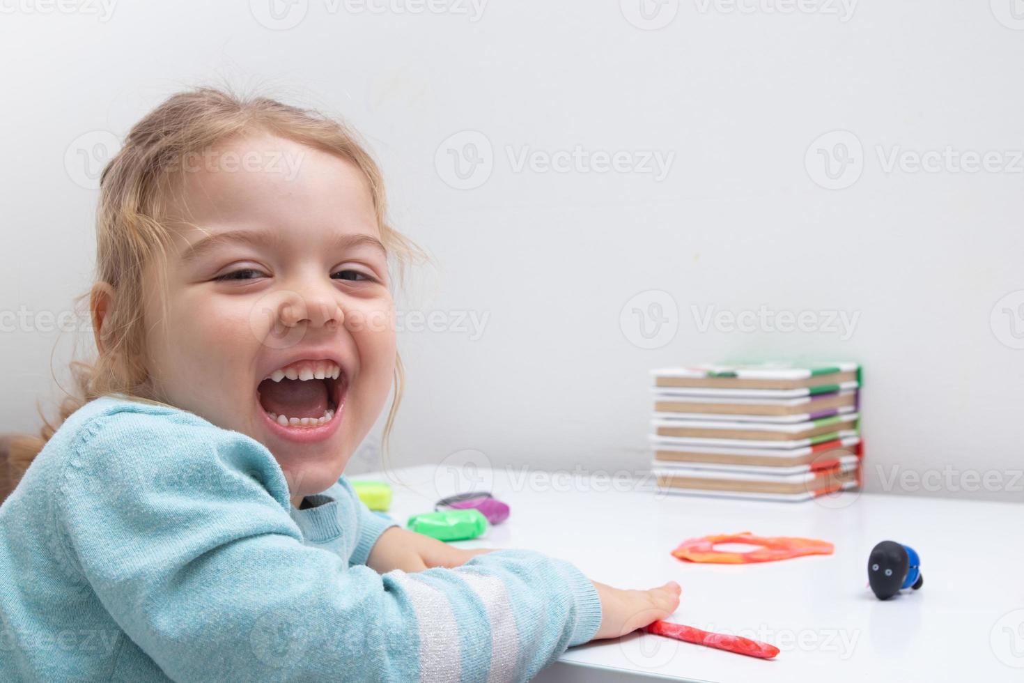 A cheerful girl at the table plays with modeling dough. Childrens games for fine motor skills photo