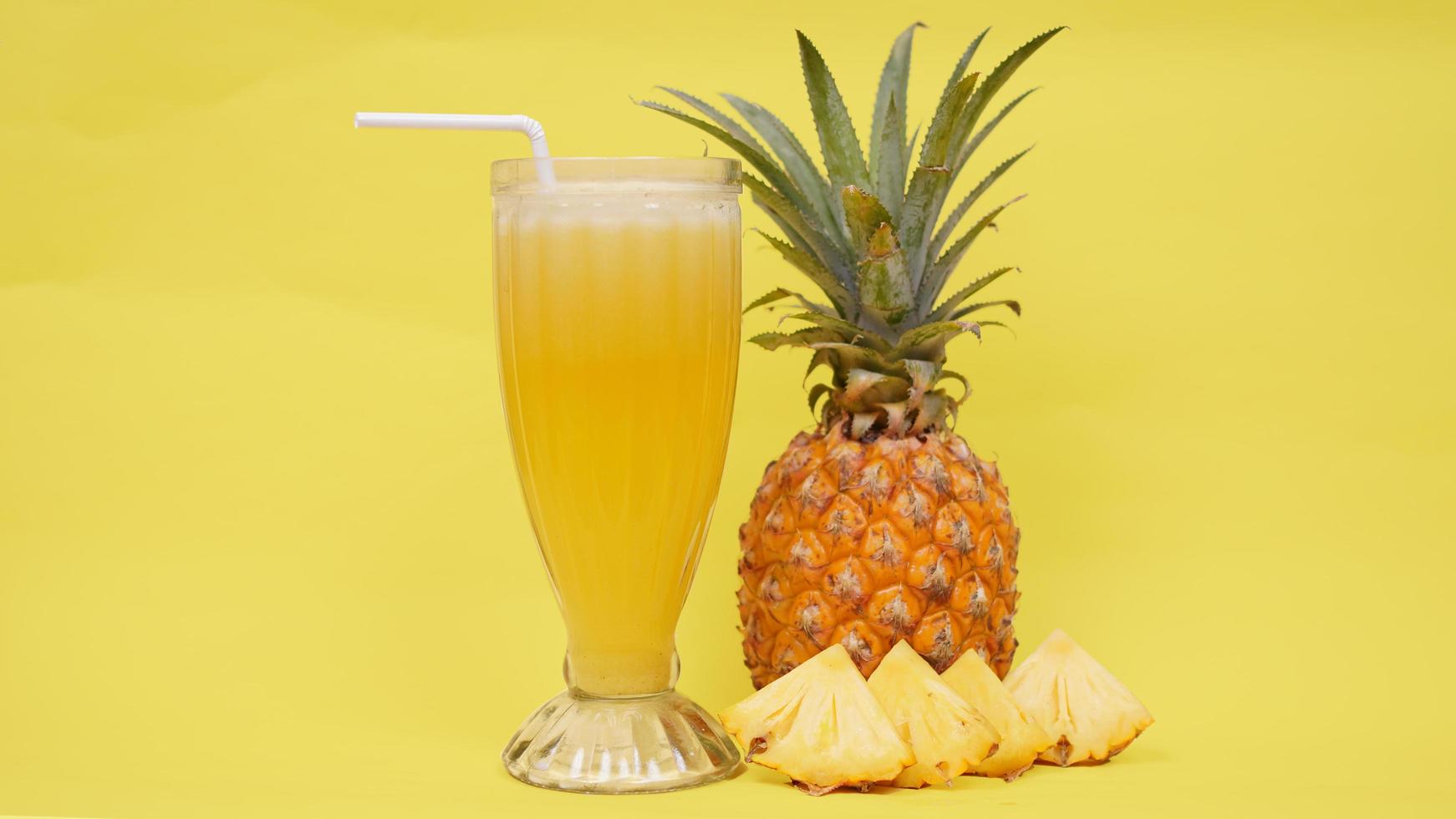 fruta de piña y un vaso de jugo aislado en un fondo amarillo foto