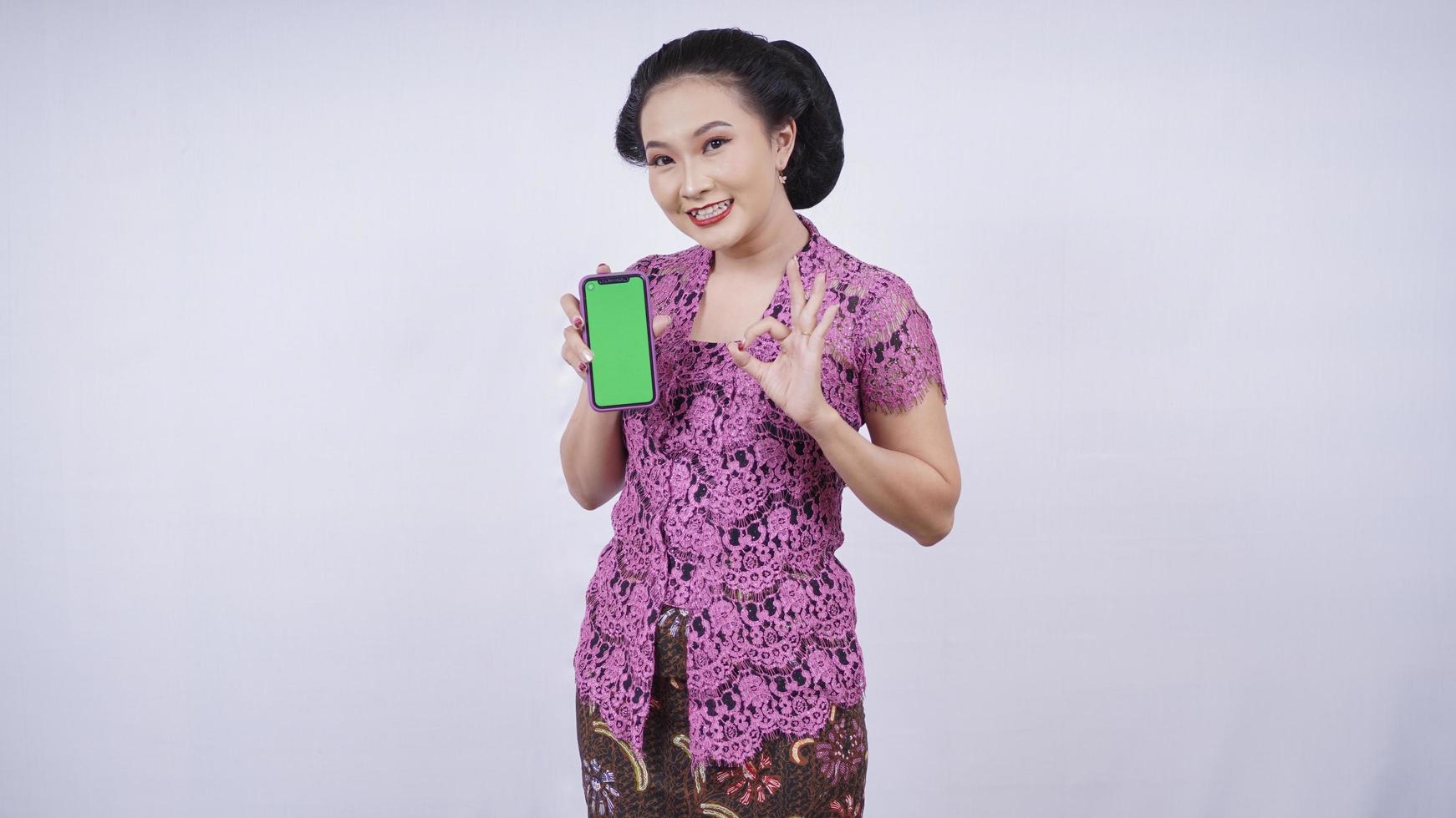 beauty in kebaya smiling showing smartphone screen ok gesture isolated on white background photo