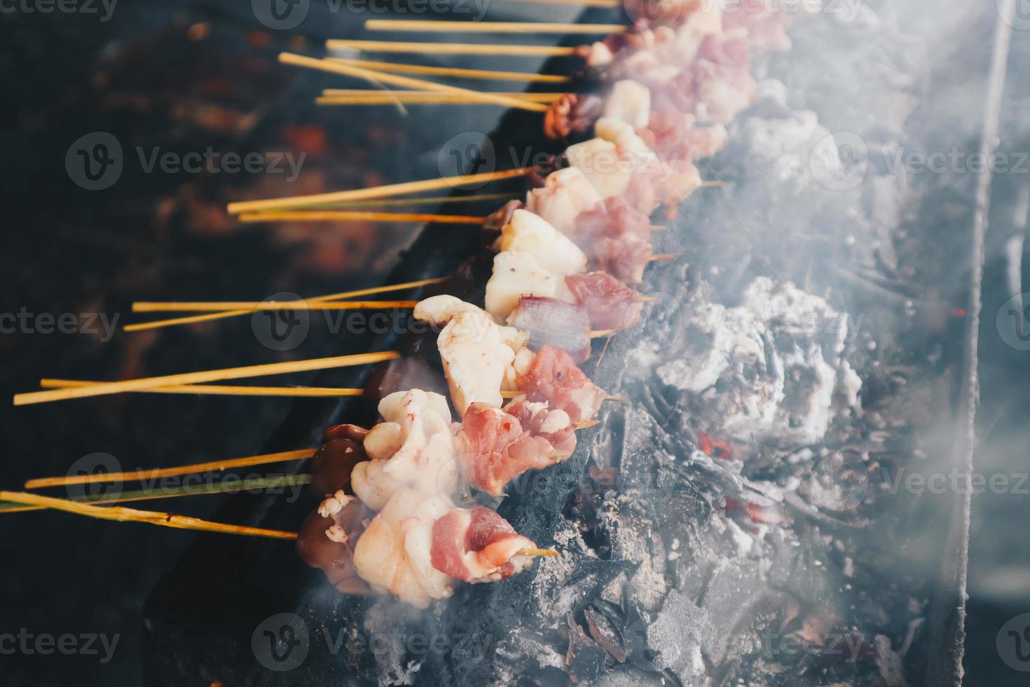 satay de cabra cruda, satay de cordero, satay de cordero o carne de cabra en un lugar de parrilla con fuego y humo. satay tradicional de java, indonesia. foto