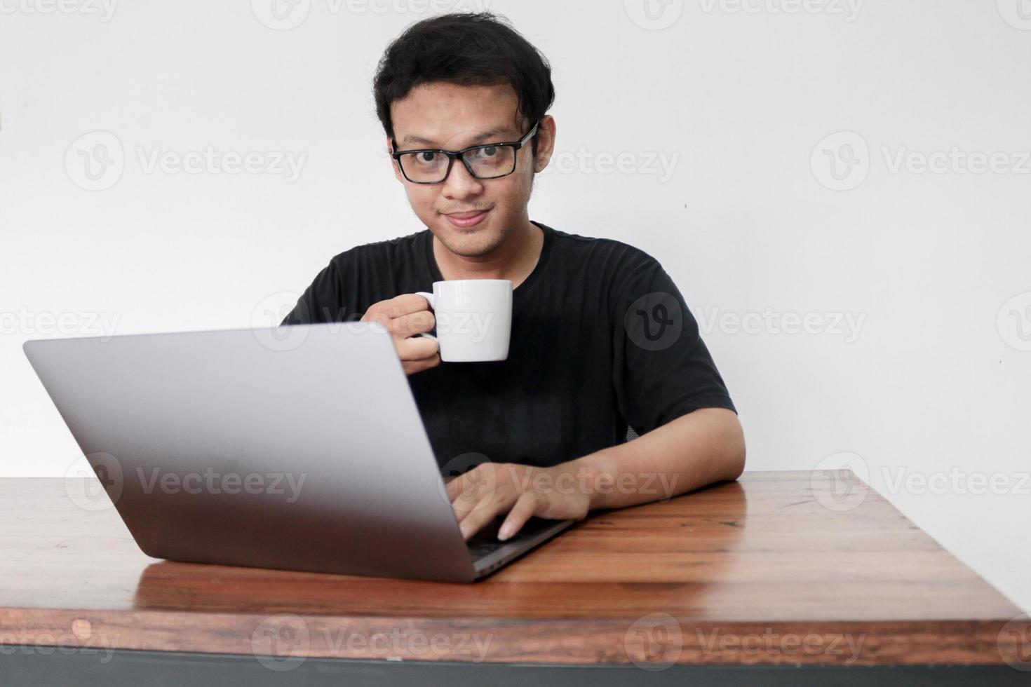 Young asian man is smile and enjoy when working at home with laptop and a cup of coffee. A man sitting on bed and working. Work from home concept photo
