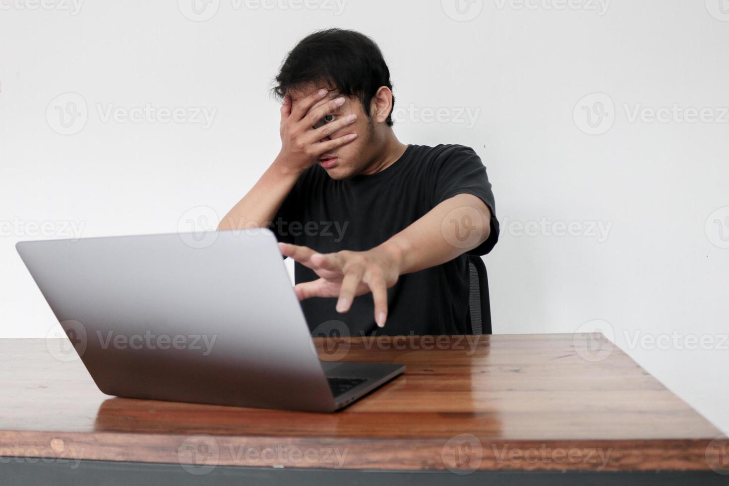 Young asian man hiding his face with hand because shocked and embarrassed by some porn videos or another forbidden thing he saw on the internet using a laptop photo