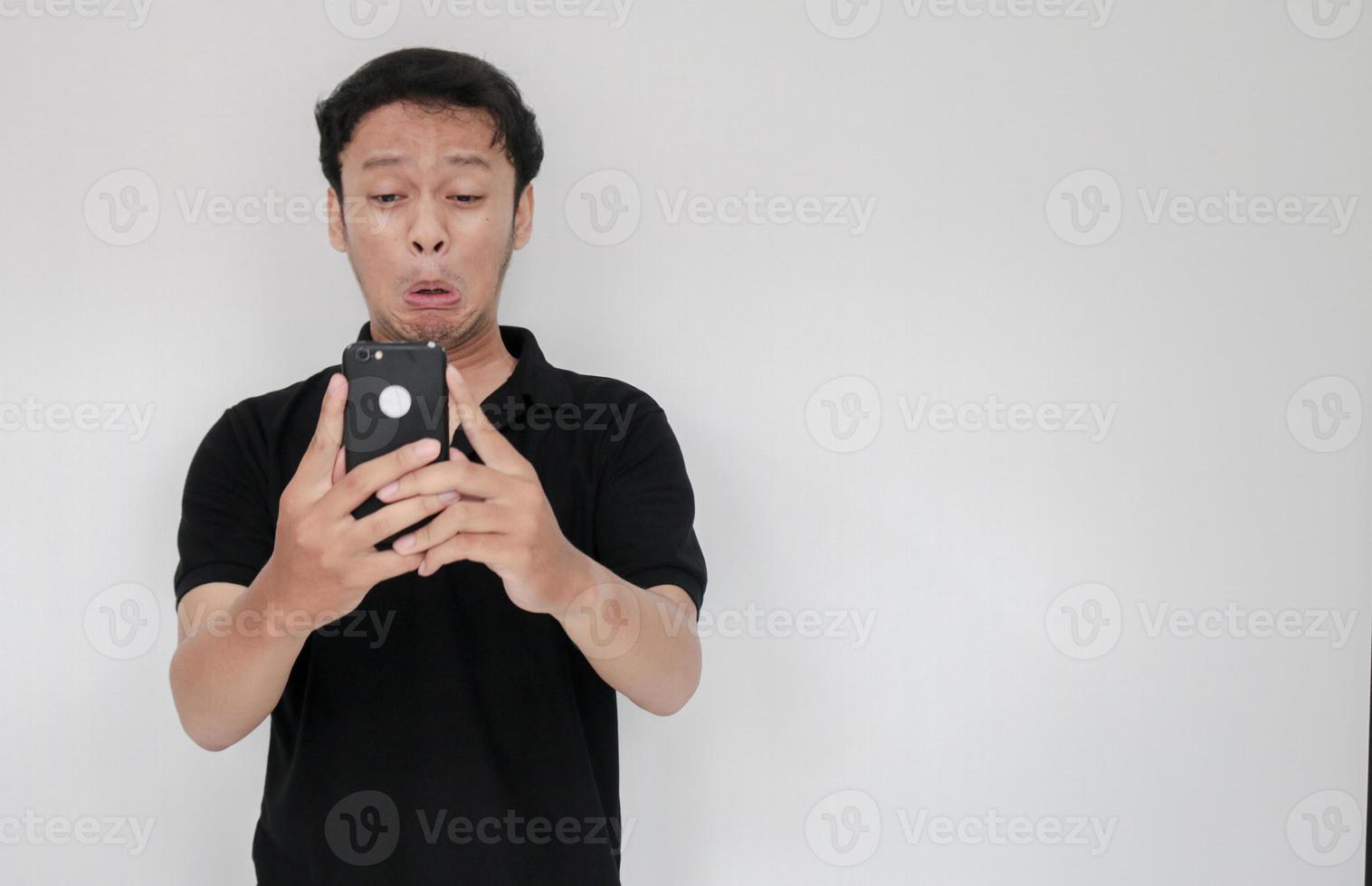 Young Asian man cry and sad when looking on the smartphone. Indonesia Man wear black shirt Isolated grey background photo