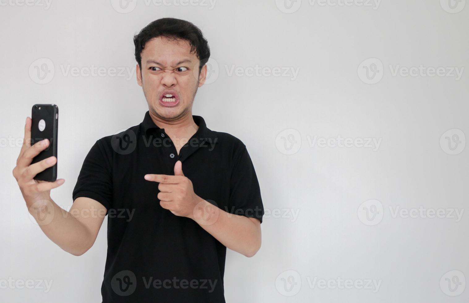 Angry Asian young man get mad on the smartphone. Indonesia Man wear black shirt Isolated grey background photo