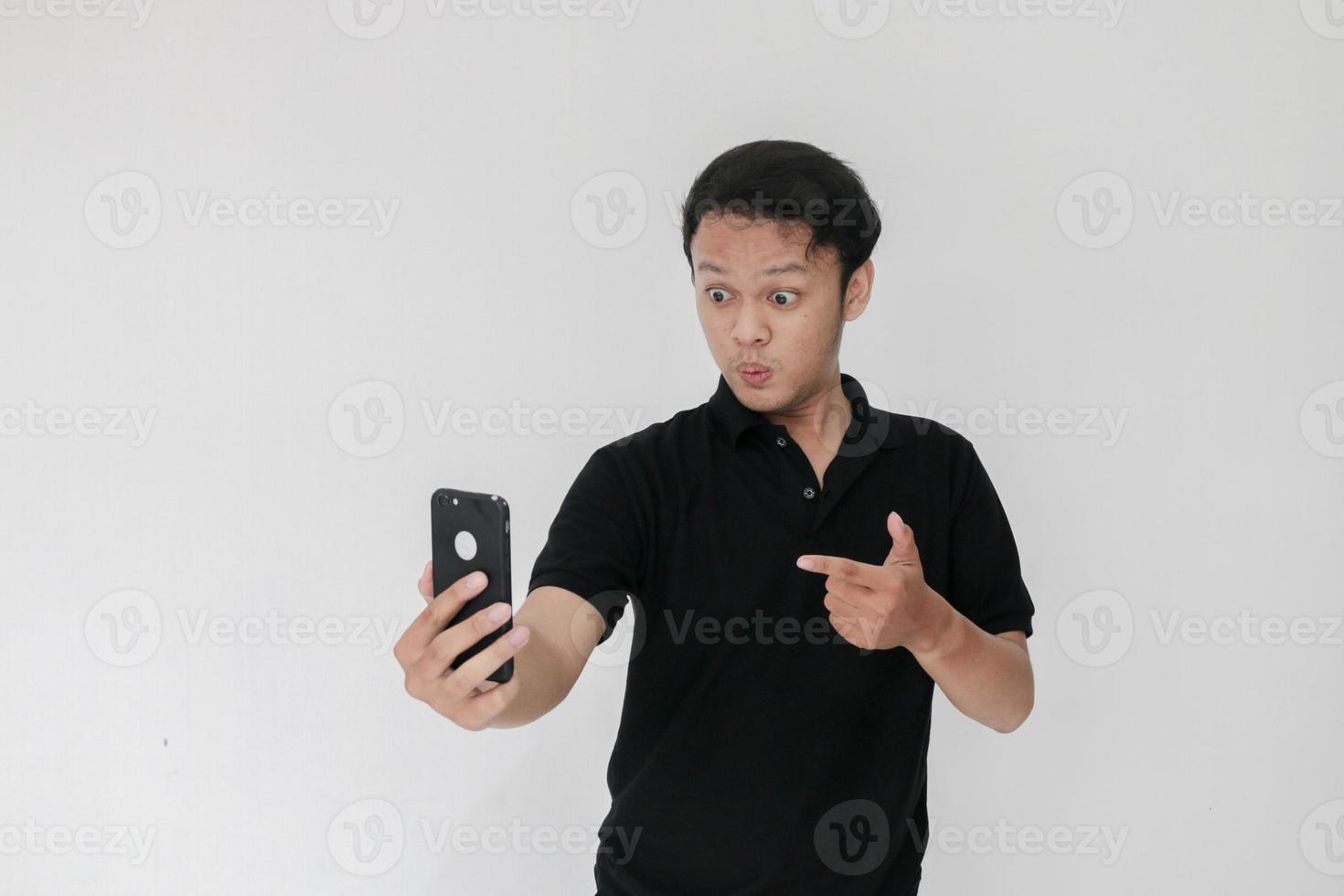 Wow face of Your Asian man shocked what he see in the smartphone on isolated grey background. Indonesia Man wear black shirt Isolated grey background photo