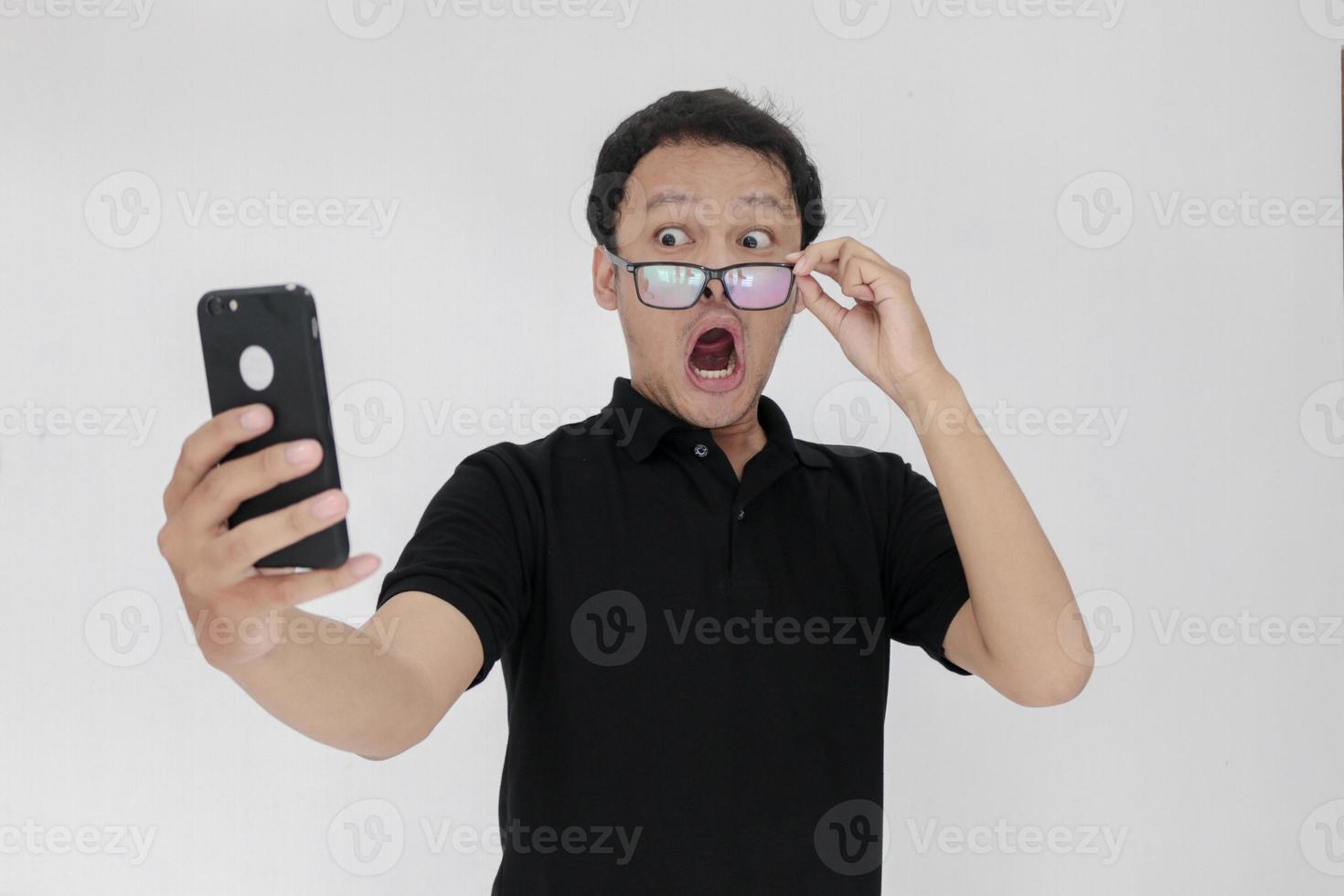 Wow face of Your Asian man shocked what he see in the smartphone on isolated grey background. Indonesia Man wear black shirt Isolated grey background photo