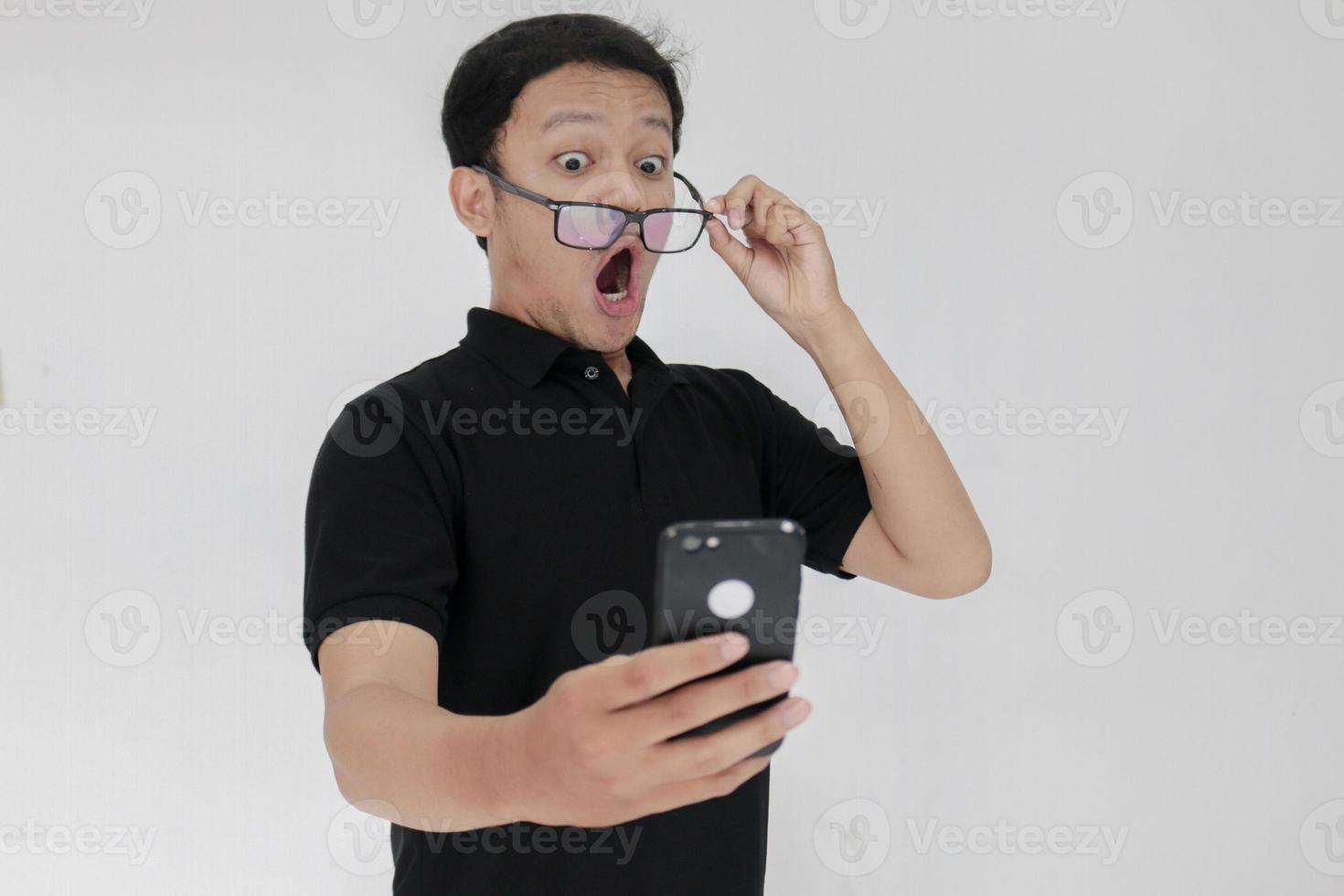 Wow face of Your Asian man shocked what he see in the smartphone on isolated grey background. Indonesia Man wear black shirt Isolated grey background photo