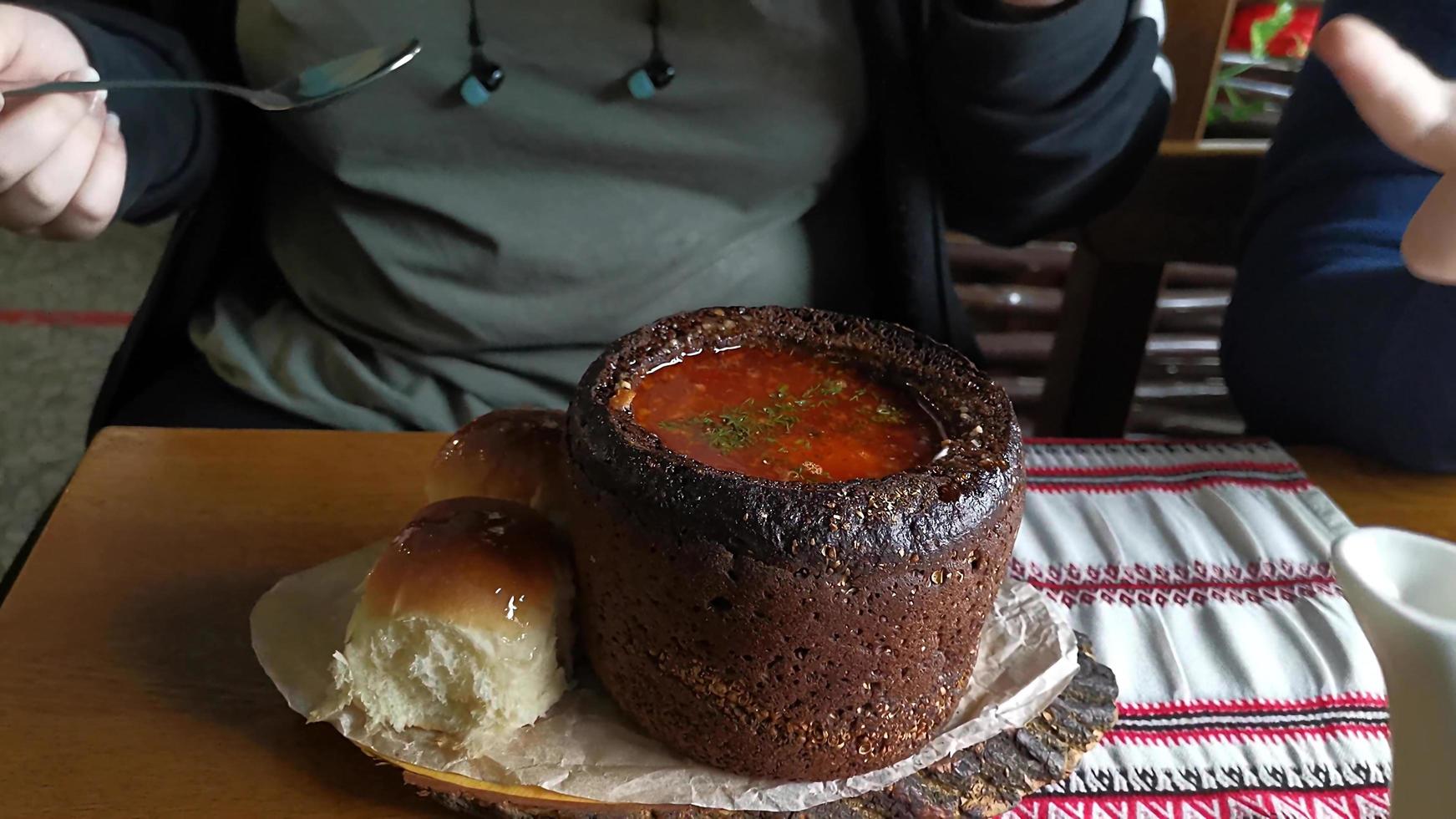 Borscht in a loaf of black bread in a cafe against the background of people photo