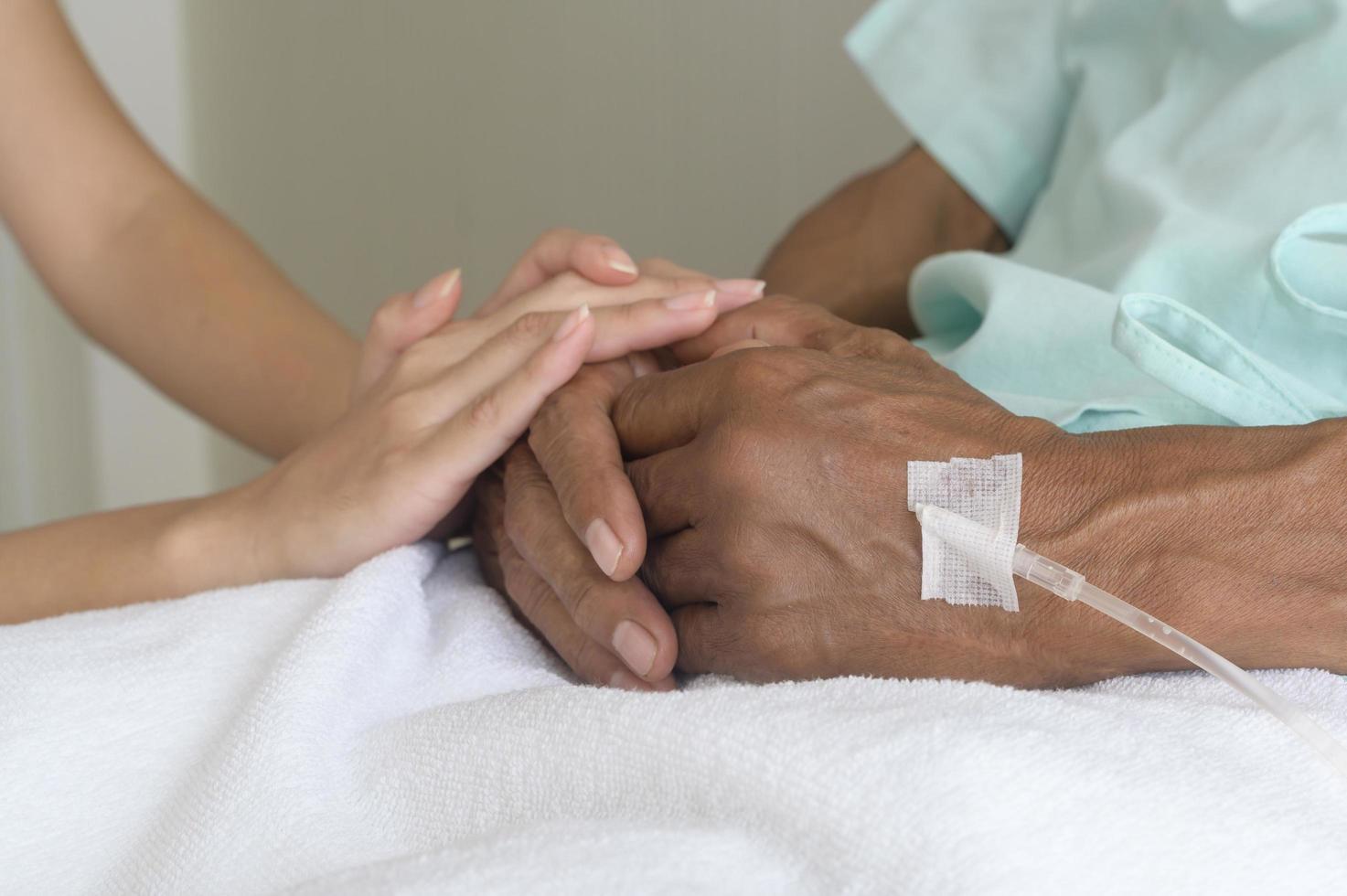 Close up of visitor holding senior patient's hand in hospital, health care and medical concept photo