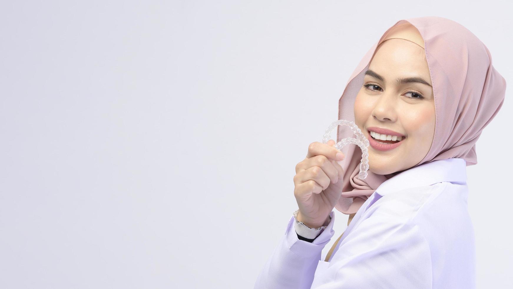 Muslim female dentist holding invisalign braces over white background studio, dental healthcare and Orthodontic concept. photo