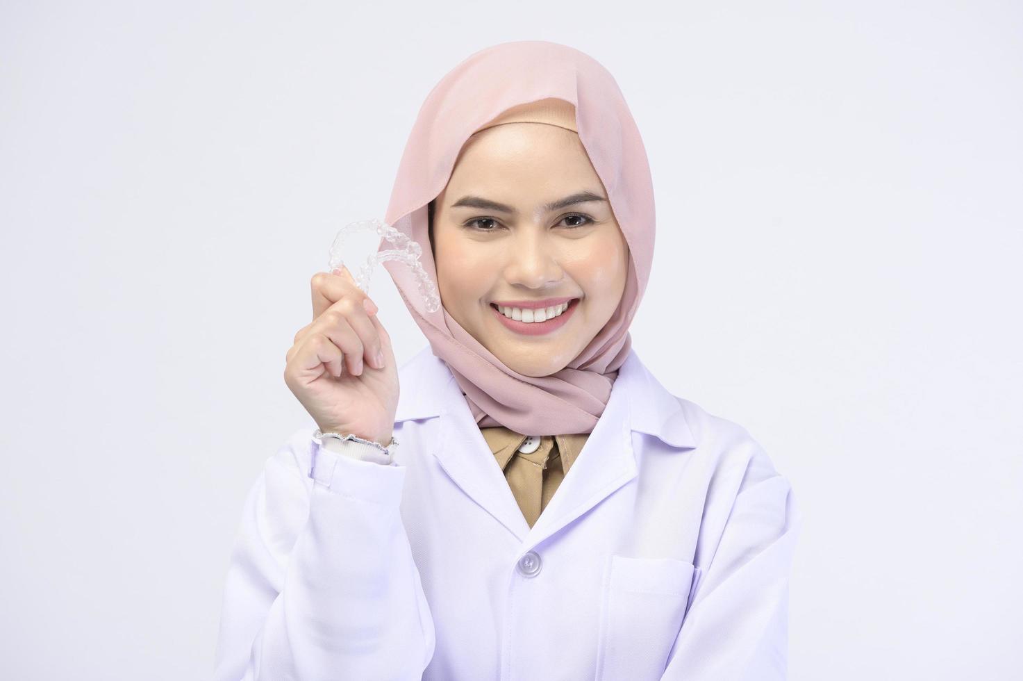 Muslim female dentist holding invisalign braces over white background studio, dental healthcare and Orthodontic concept. photo