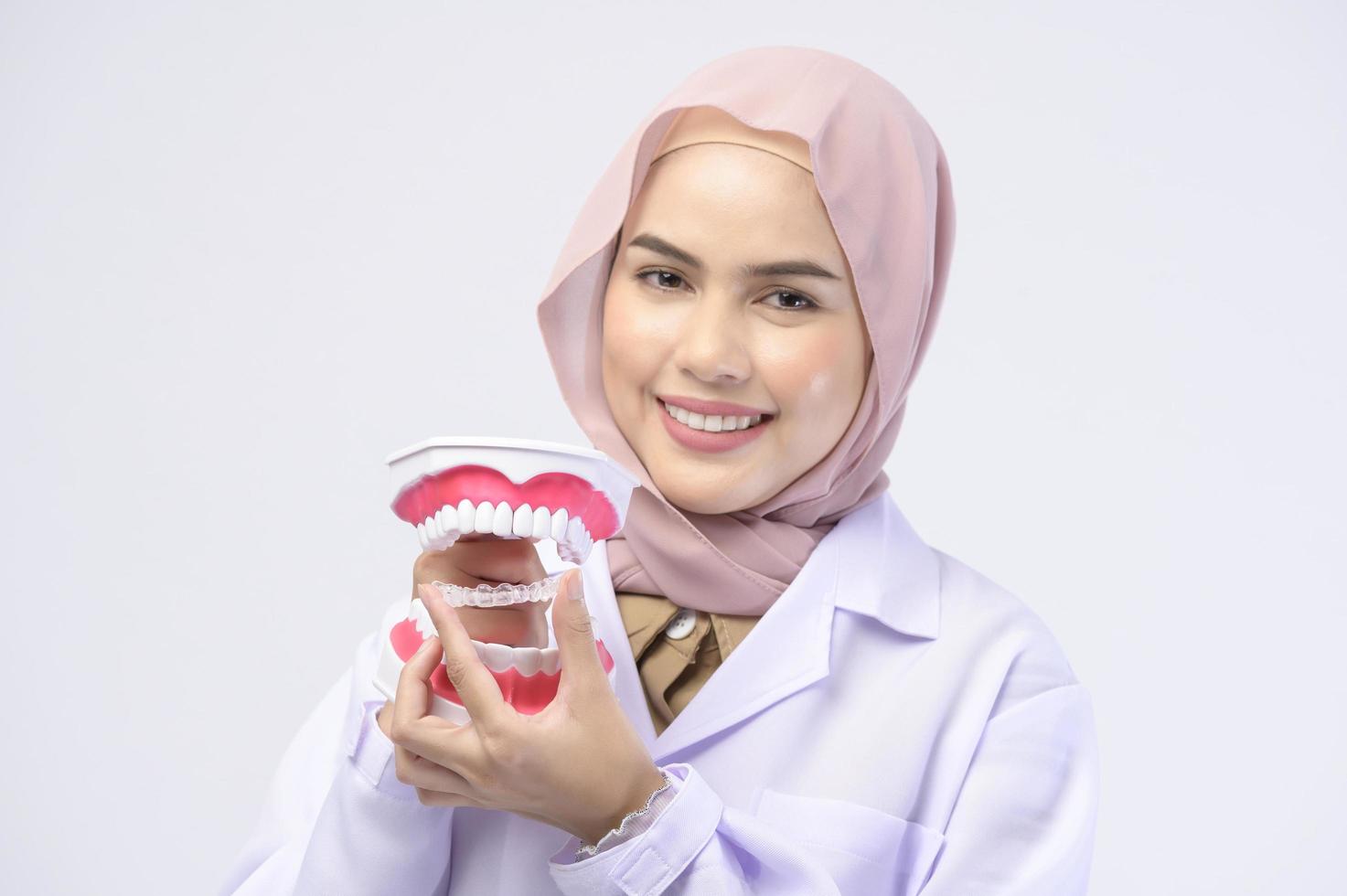 Muslim female dentist holding invisalign braces over white background studio, dental healthcare and Orthodontic concept. photo