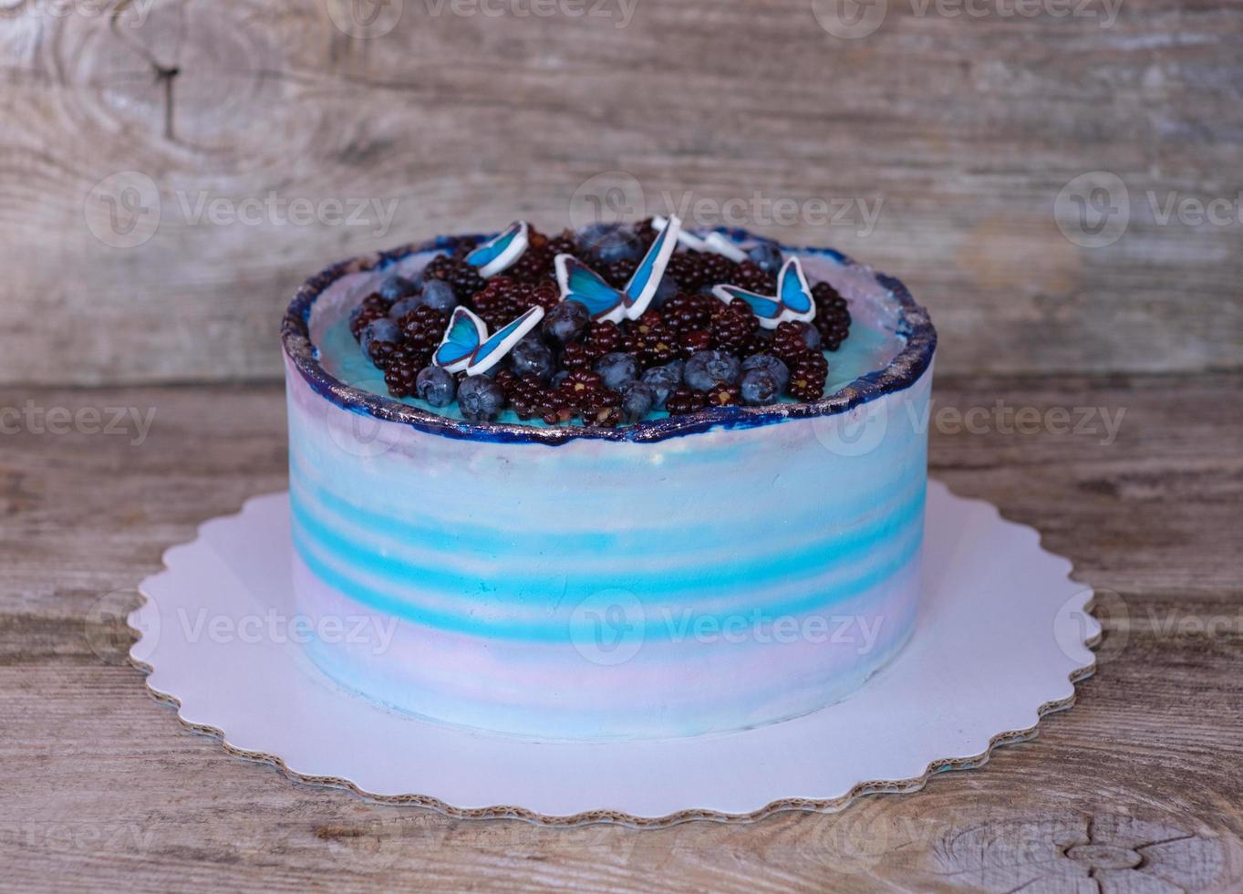 hermoso pastel casero con crema morada y azul, decorado con moras, arándanos y mariposas foto