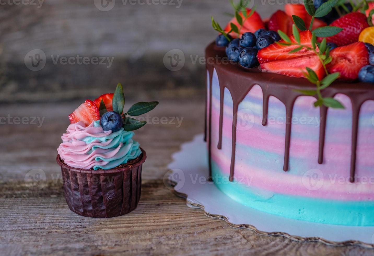 homemade cupcakes with pink and turquoise cream, decorated with strawberries and blueberries photo