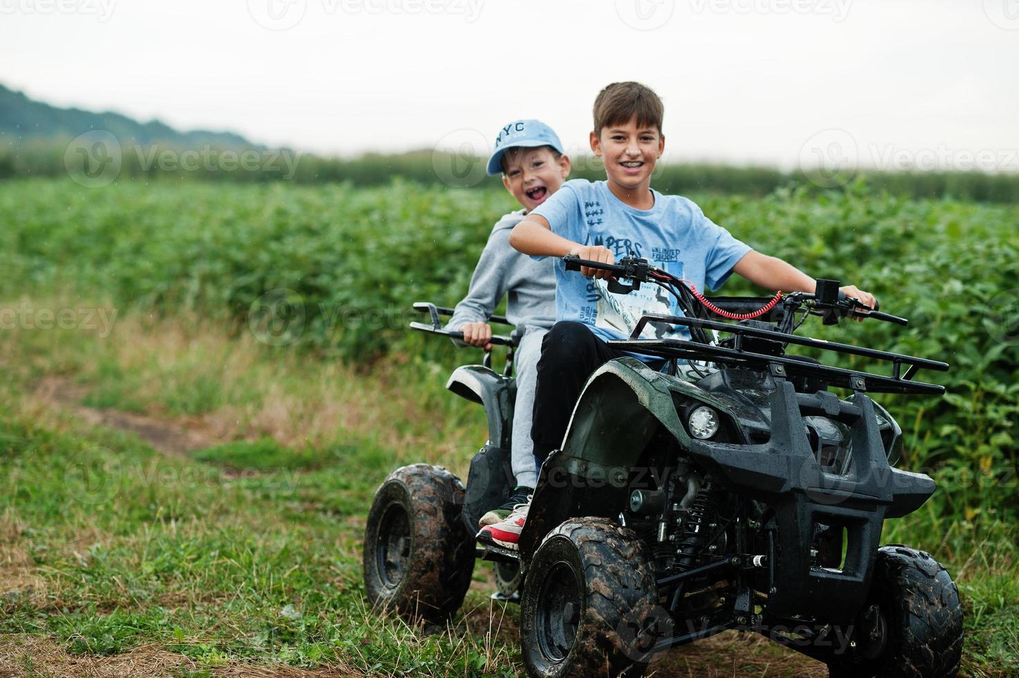 Two brothers driving four-wheller ATV quad bike. Happy children moments. photo