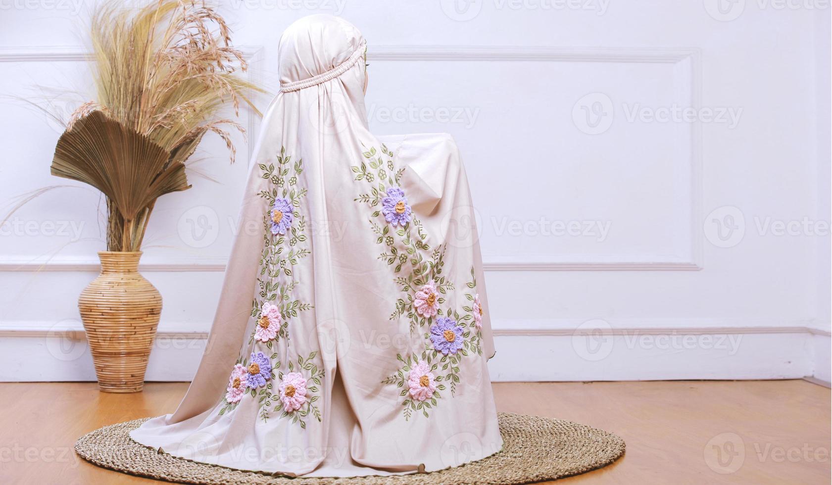 A Muslim woman wearing moslem clothes with hijab called mukena, praying by raising her hands with minimalist home background photo