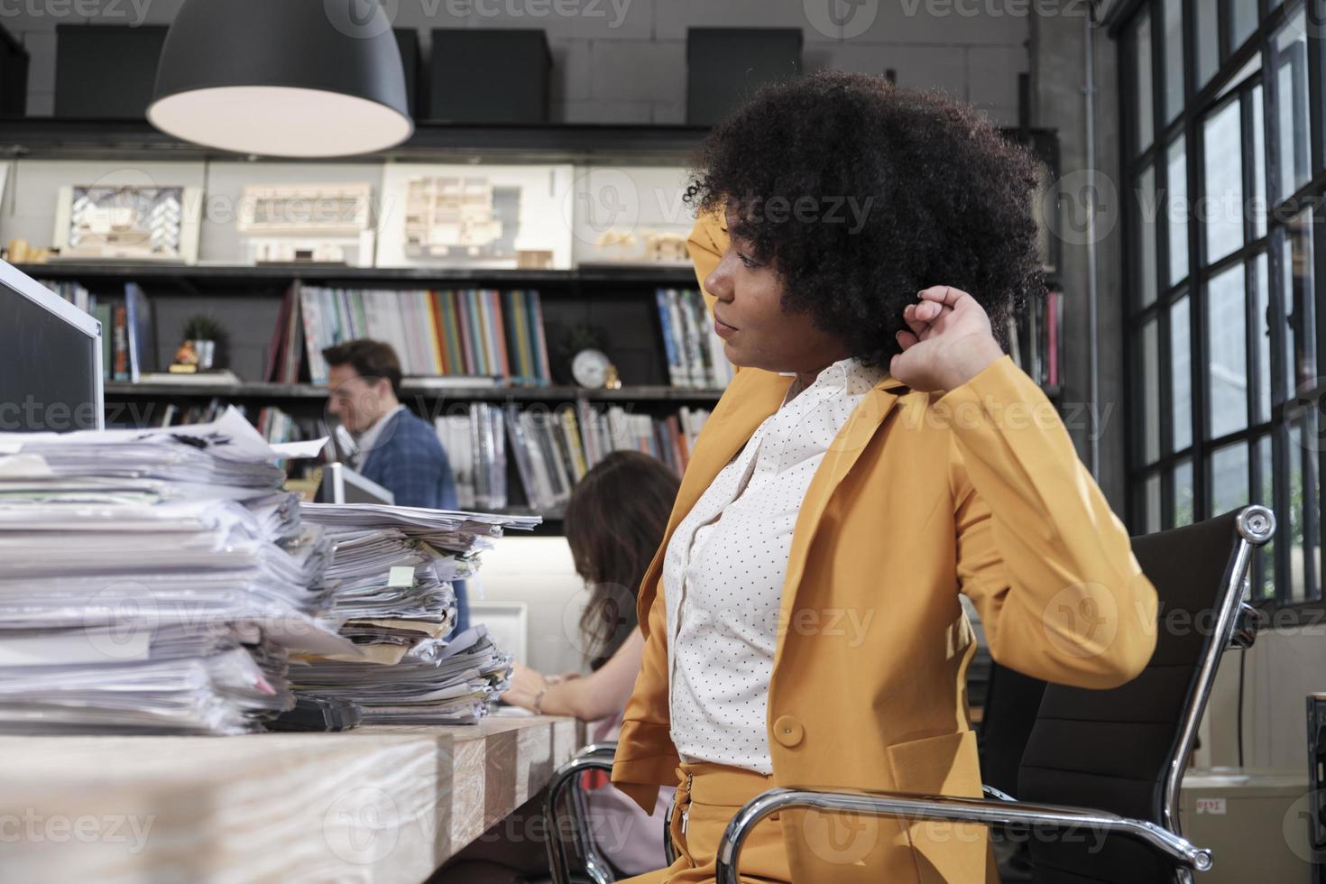 Busy female worker, young African American staff is hard working with a lot of stack of documents and paperwork on desk, overload worked tirelessly for the job deadline in business office workspace. photo