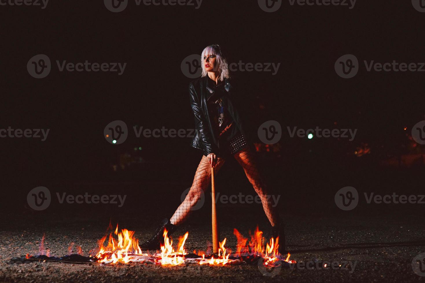 Portrait of stylish blonde grunge young woman  with the club near the fire at night photo