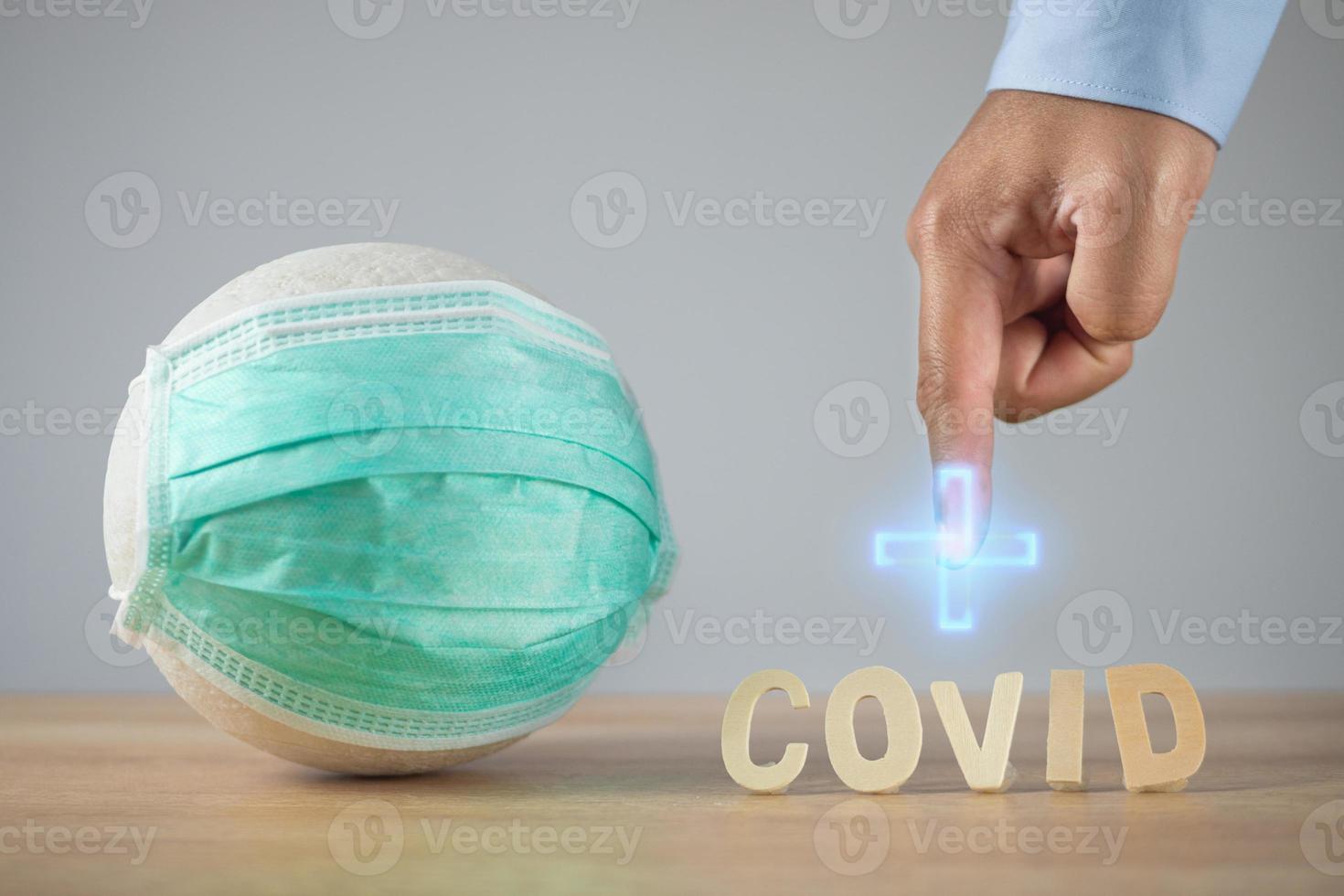 seguro de salud en concepto de covid. gráfico de cruz médica azul en el dedo del hombre. bola blanca con máscara médica verde sobre la mesa. foto