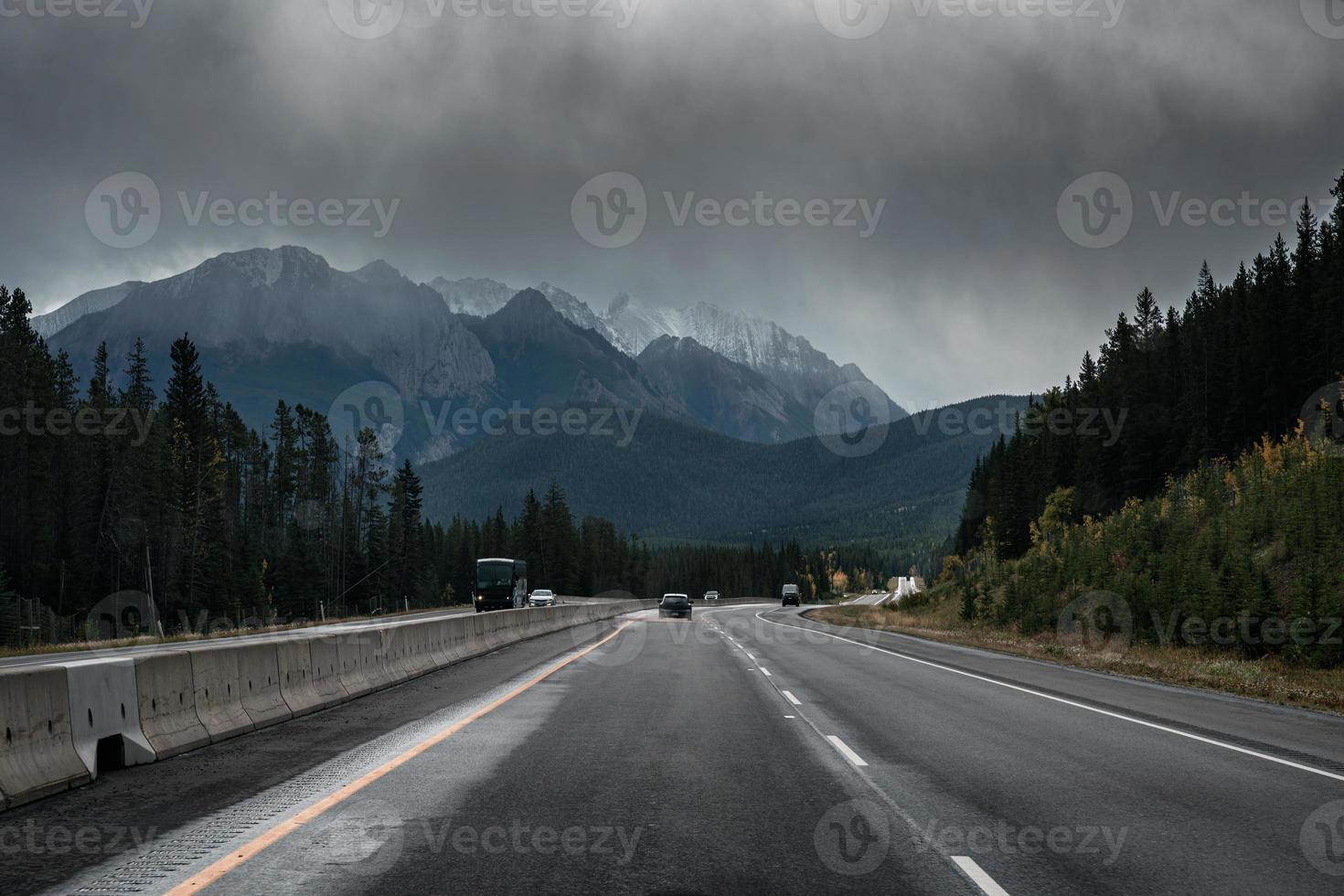 Car driving on highway with rocky mountains and moody sky in overcast day at Banff national park photo