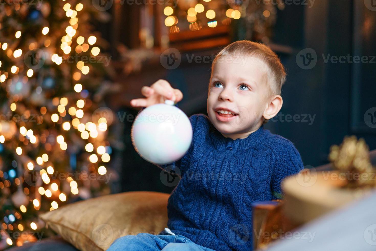 Happy little boy sitting on sofa with christmas tree decoration in cozy living photo