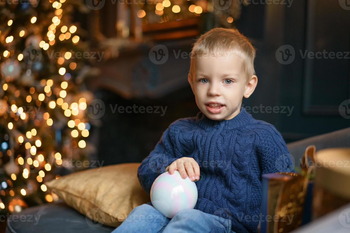 cute boy sitting on the couch in the background of Christmas tree. photo