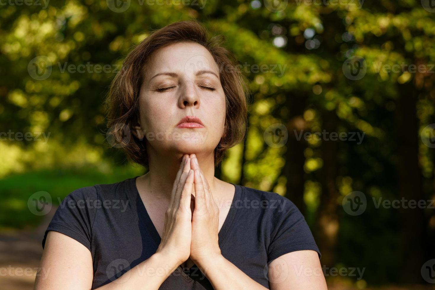adult woman meditates with folded palms in the park with closed eyes photo