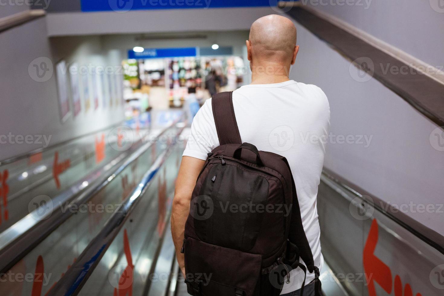 Bald man walking down the escalator with a backpack photo