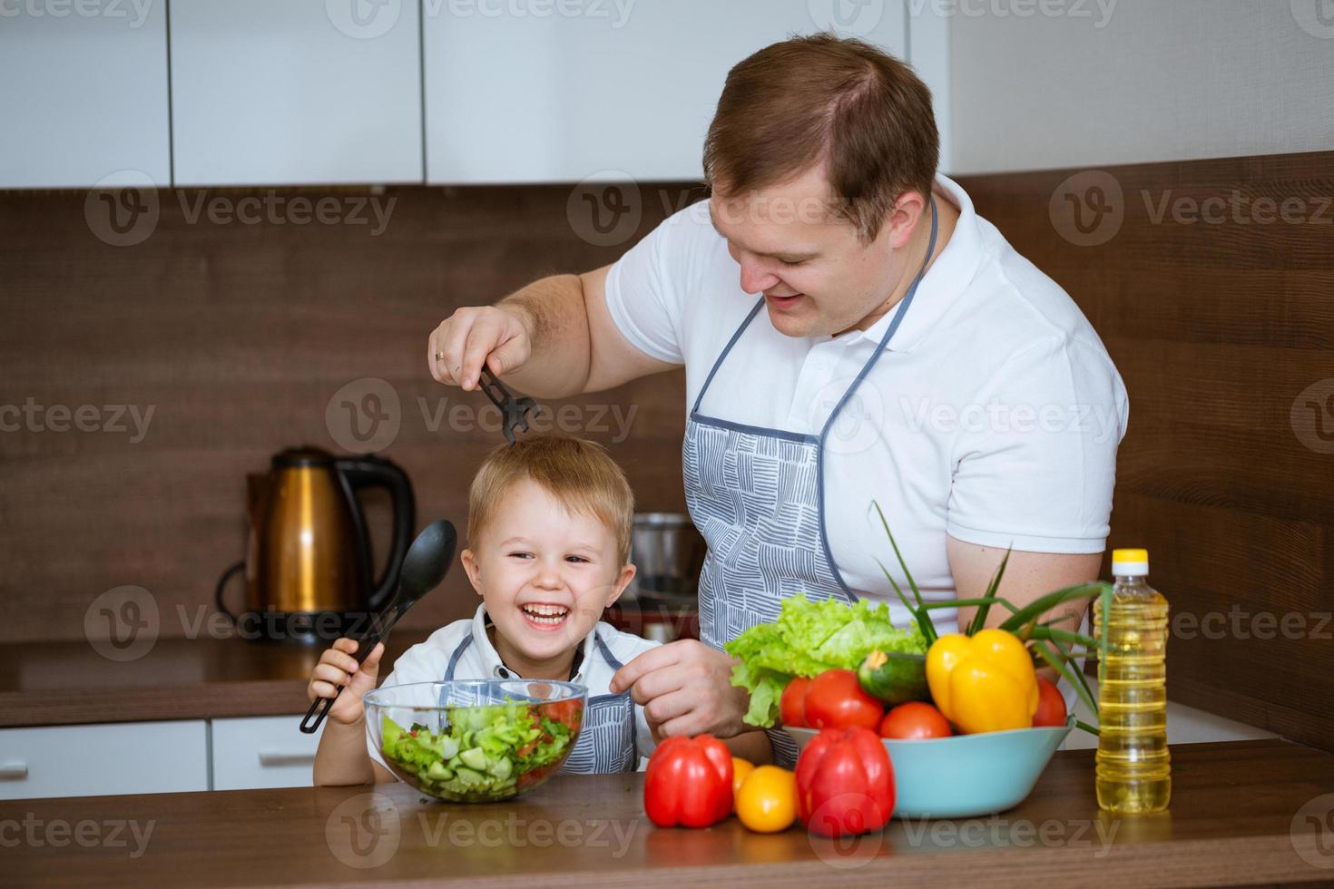 hijo y padre preparan ensalada juntos en la cocina foto
