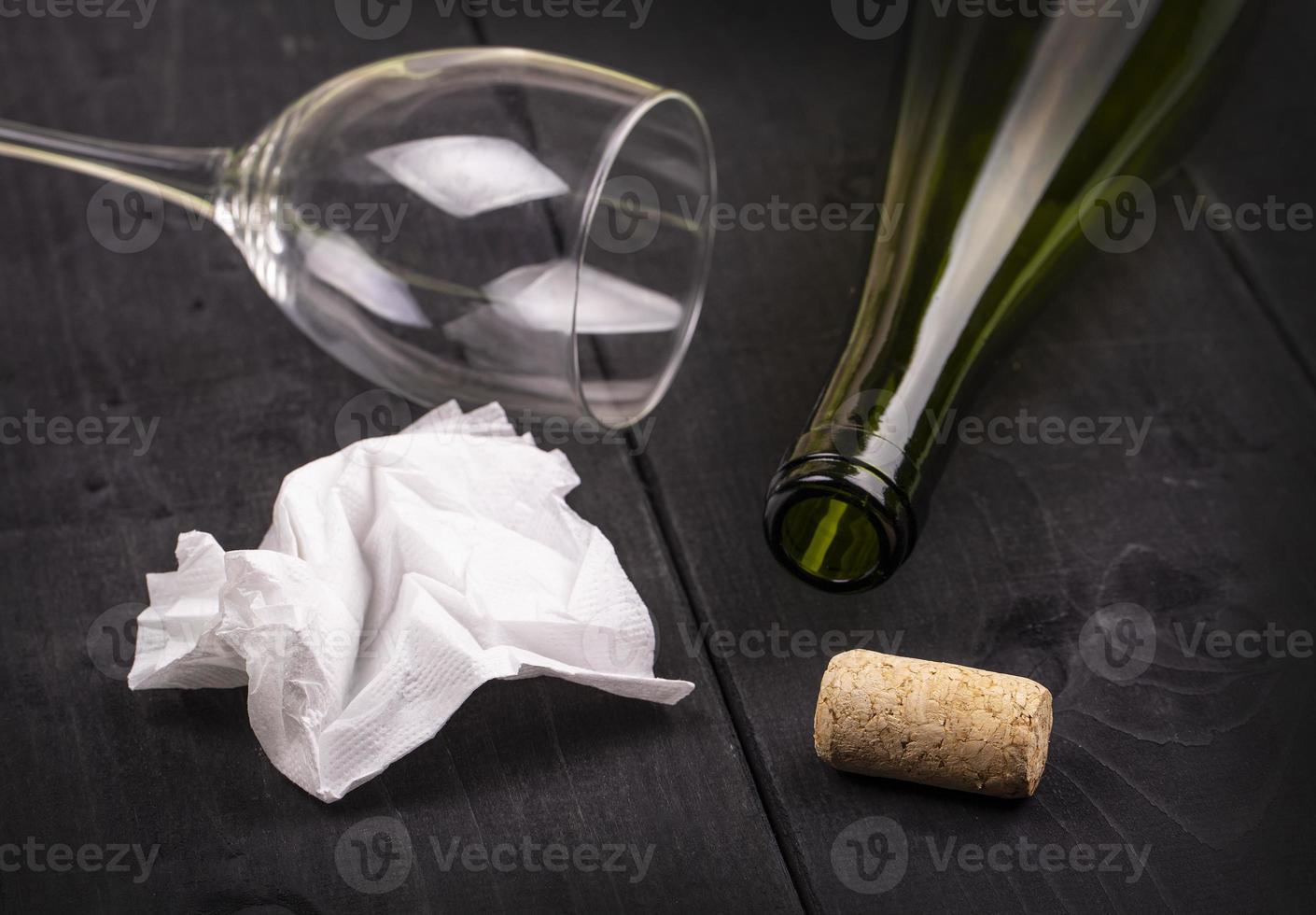 The used white crumpled paper napkin and an empty wine bottle with cork on old wooden table photo