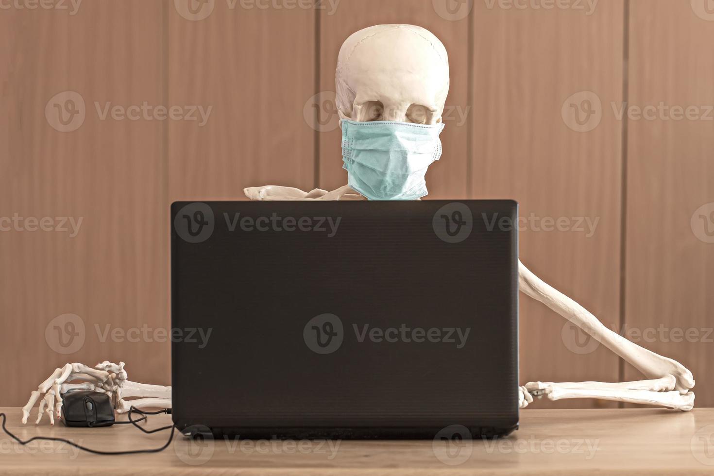 skeleton in protective medical mask works with the laptop photo