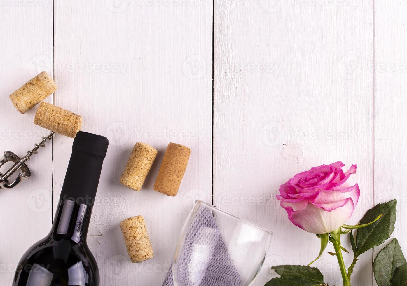 The Glass bottle of wine with corks and rose on white wooden table photo