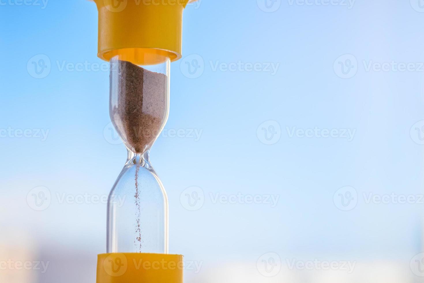 The sizzling sand in the hourglass against the blue sky. photo