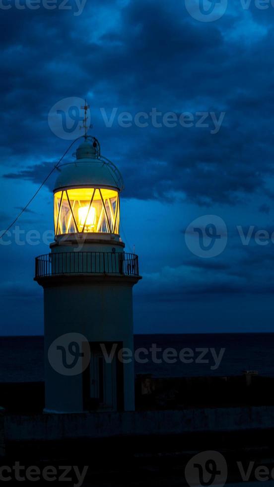 el faro brillando en la noche oscura en la costa españa foto