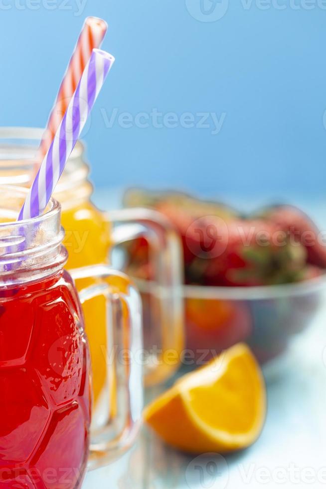 The two cups with orange juice and strawberries on blue background photo