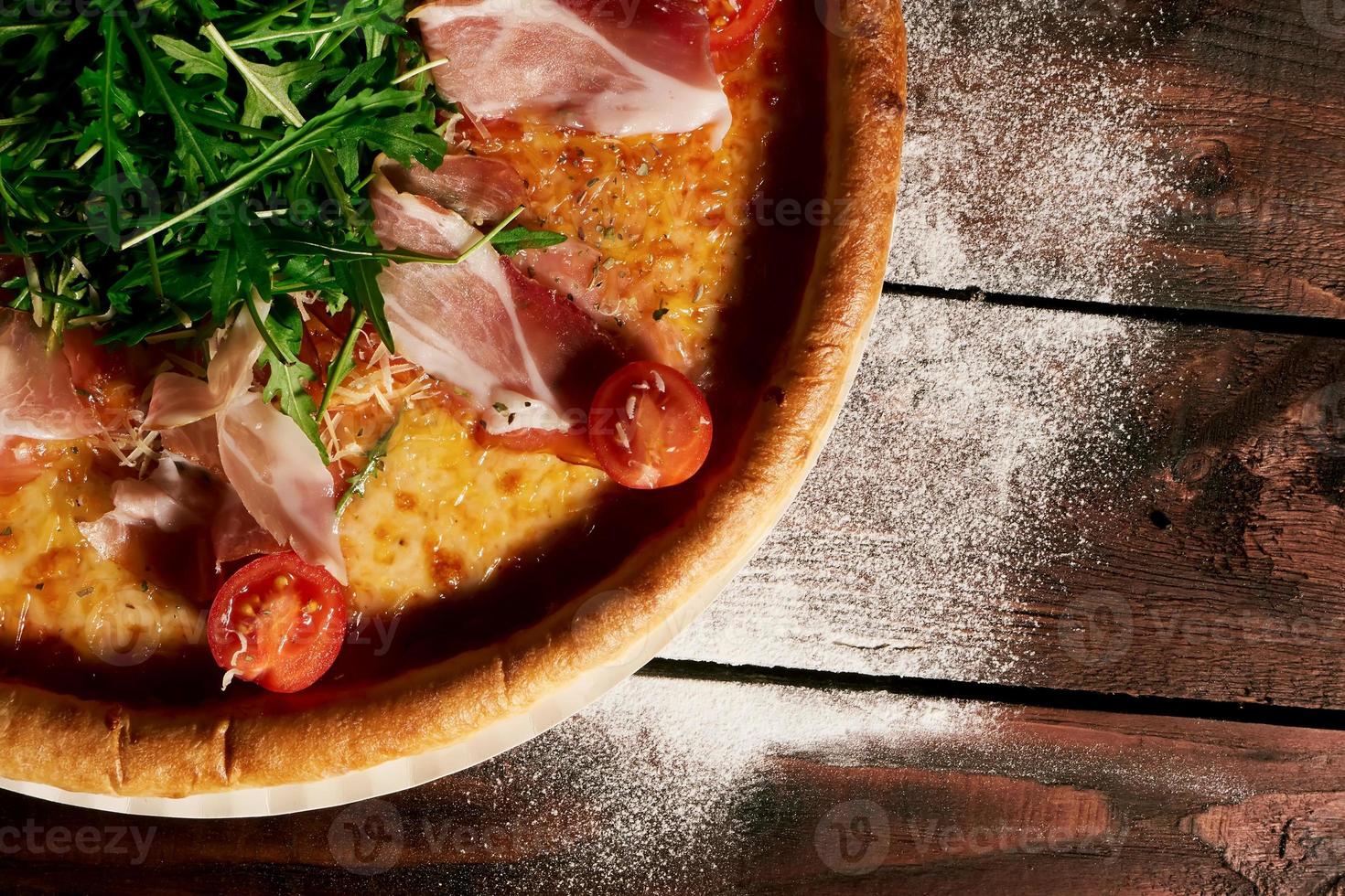 Italian pizza with ham, tomatoes and herbs on a wooden table photo