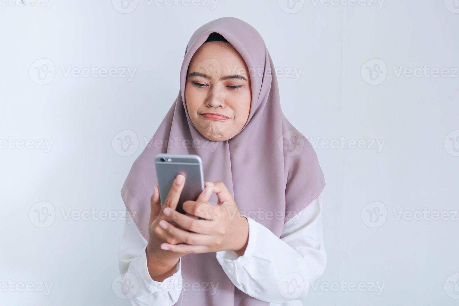 Young Asian Islam woman wearing headscarf is sad and cry in what she see on the smartphone. Indonesian woman on gray background photo