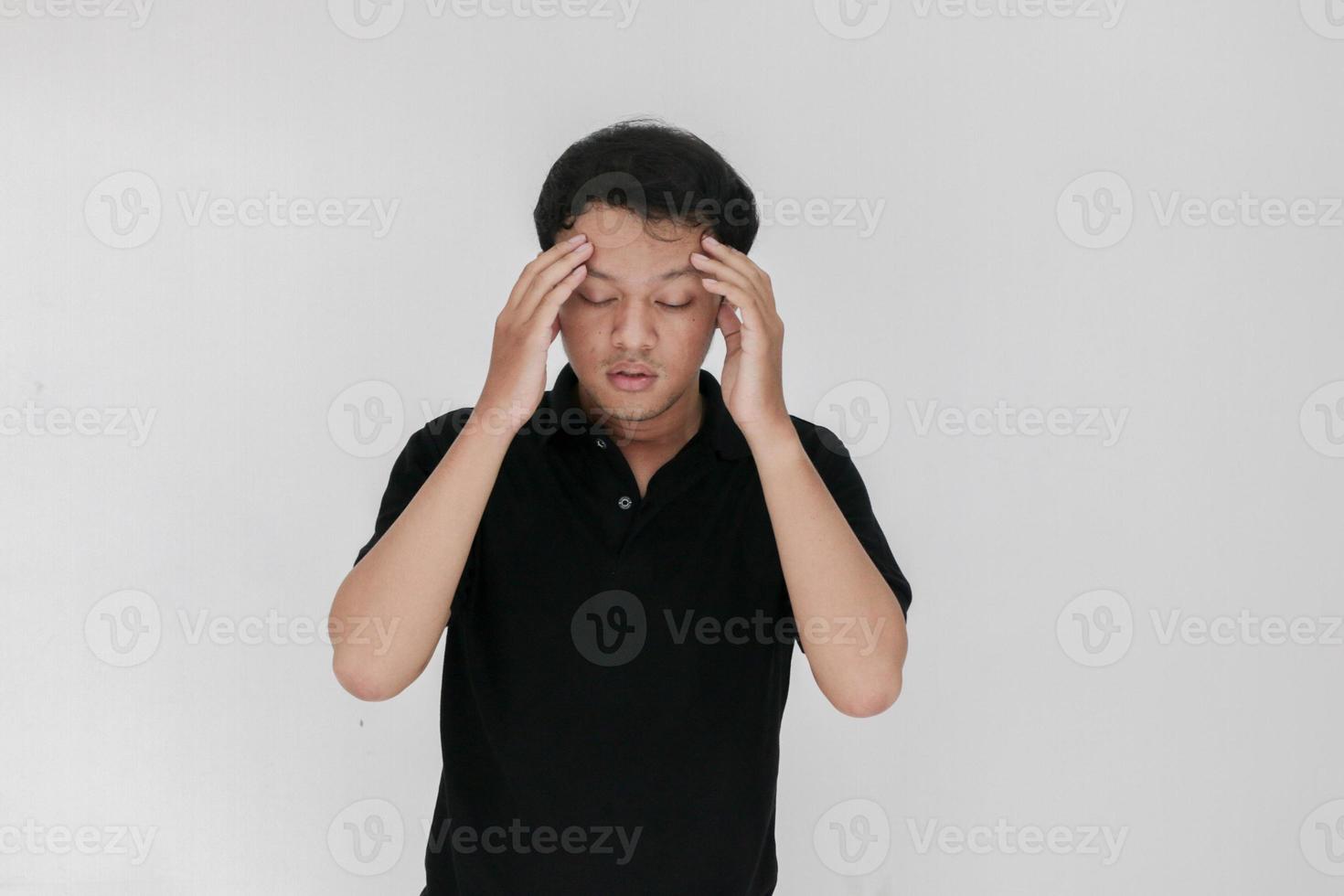 Portrait of young asian man isolated on grey background suffering from severe headache, pressing fingers to temples, closing eyes to relieve pain with helpless face expression photo