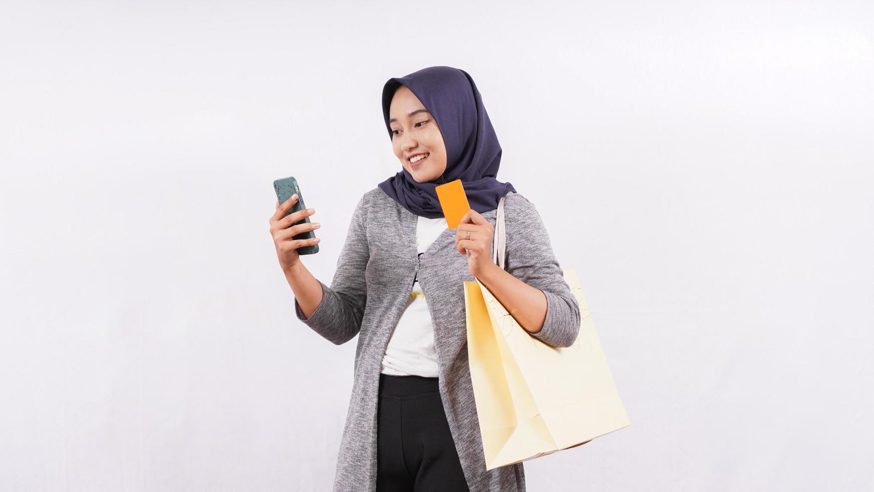 Chica asiática y bolsa de compras con teléfono inteligente y tarjeta de débito aislado sobre fondo blanco. foto