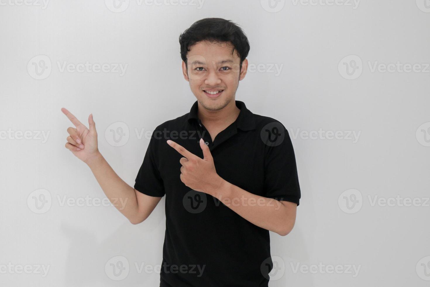 feliz y sonrisa de un joven asiático con un punto de mano en el espacio vacío. indonesia hombre usar camisa negra aislado fondo gris foto