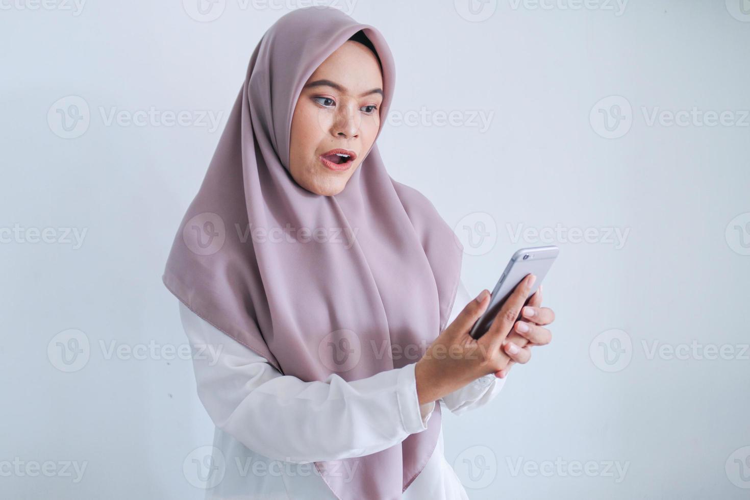 Young Asian Islam woman wearing headscarf is shocked and wow in the smartphone. Indonesian woman on gray background photo