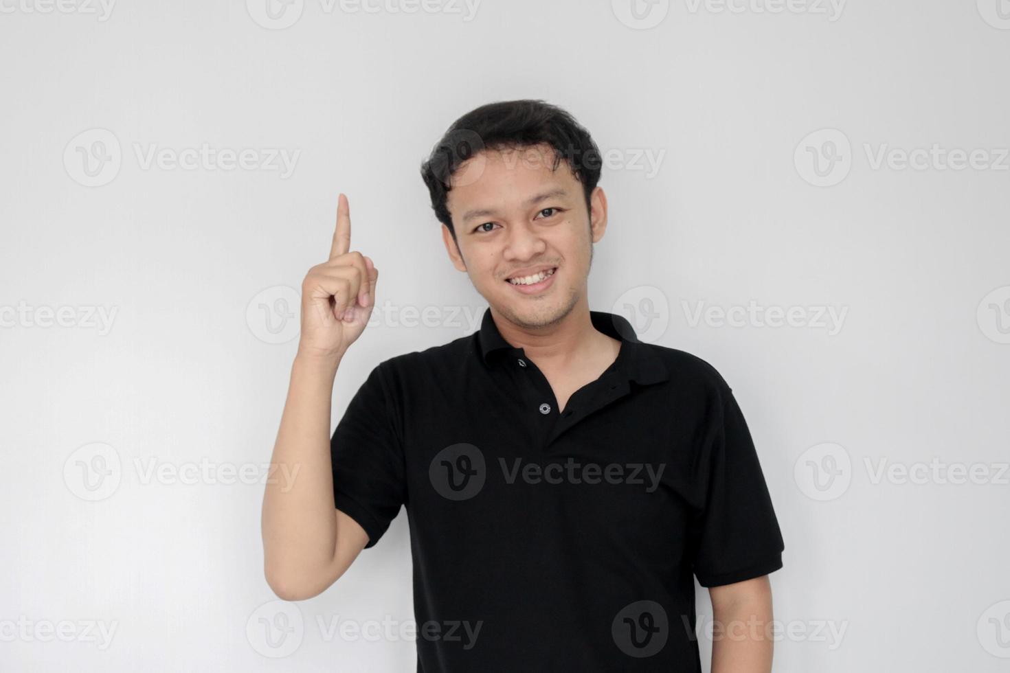 cara feliz y sonriente con sonrisa de joven asiático en camisa negra con punto de mano sobre el espacio vacío. foto