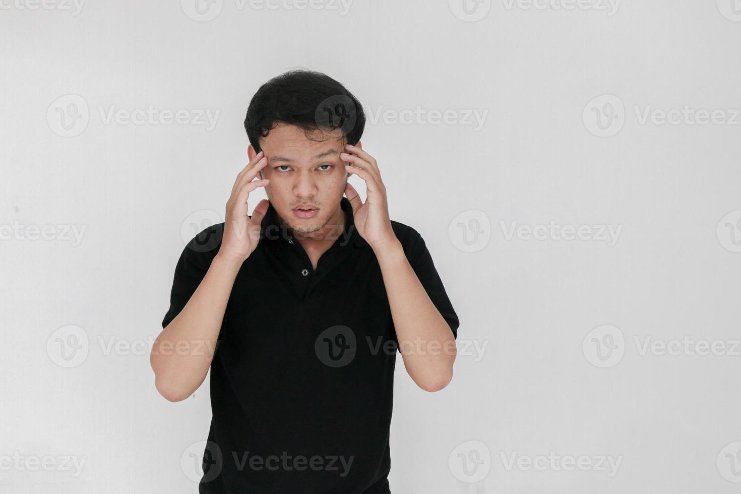 Portrait of young asian man isolated on grey background suffering from severe headache, pressing fingers to temples, closing eyes to relieve pain with helpless face expression photo