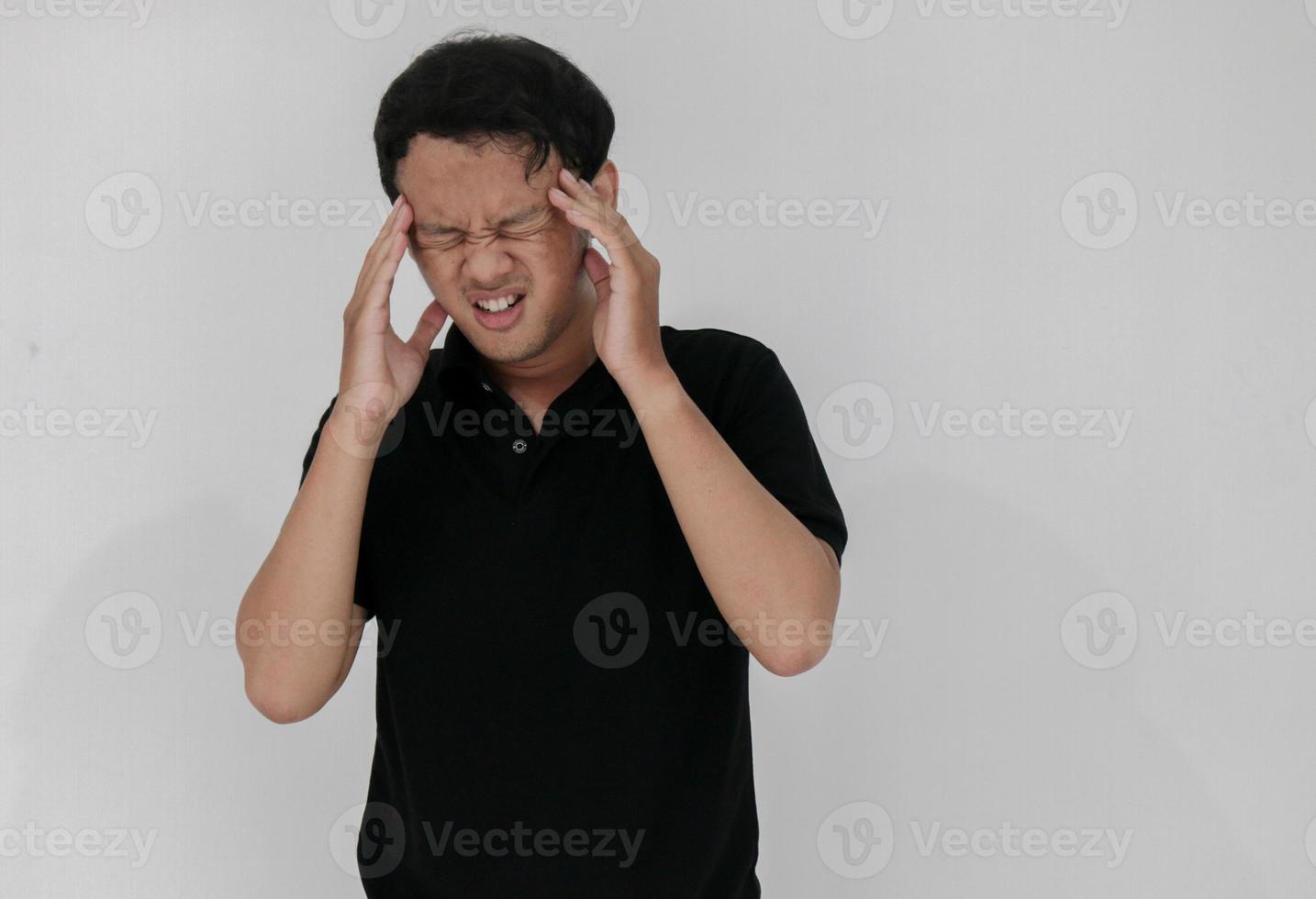 Portrait of young asian man isolated on grey background suffering from severe headache, pressing fingers to temples, closing eyes to relieve pain with helpless face expression photo