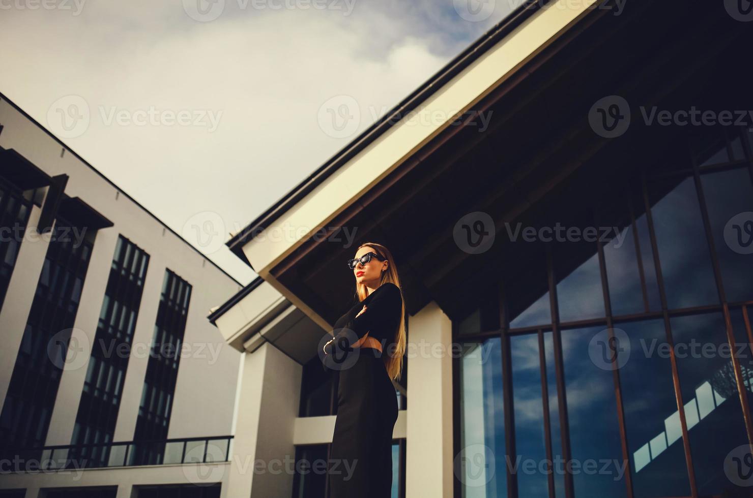 modelo atractivo en gafas de sol de pie cerca del centro de negocios foto