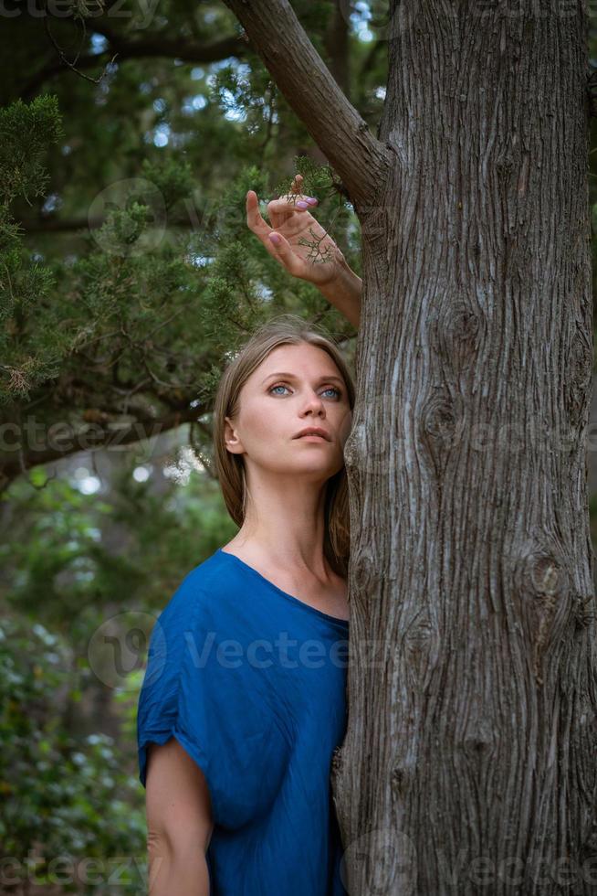 una mujer mira desde detrás de un árbol y mira a lo lejos. foto