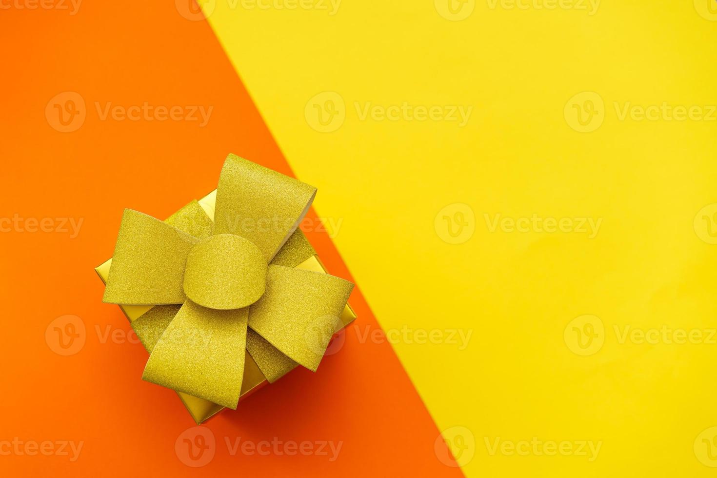 Bright yellow gift box with gold bow and ribbon on yellow and orange photo