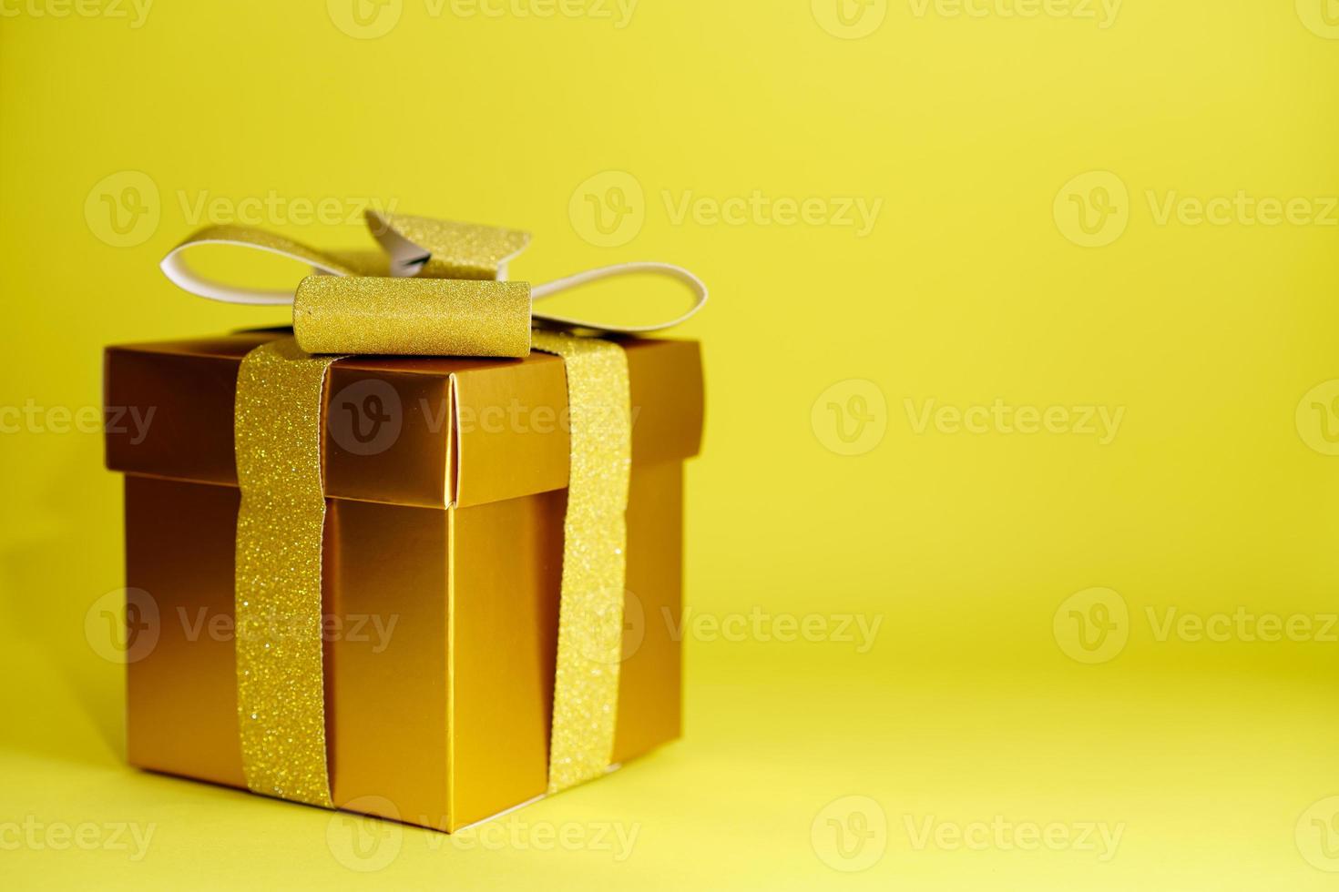 Golden box with gold paper ribbon and bow on yellow background is a universal photo