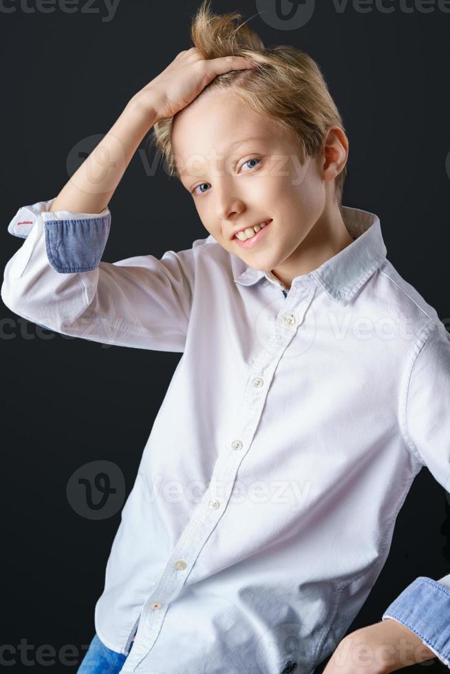 blond guy in a white shirt straightens his hair against a black background photo